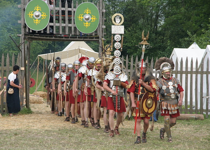 Photo of modern reenactors dressed as Roman soldiers marching out of a camp.